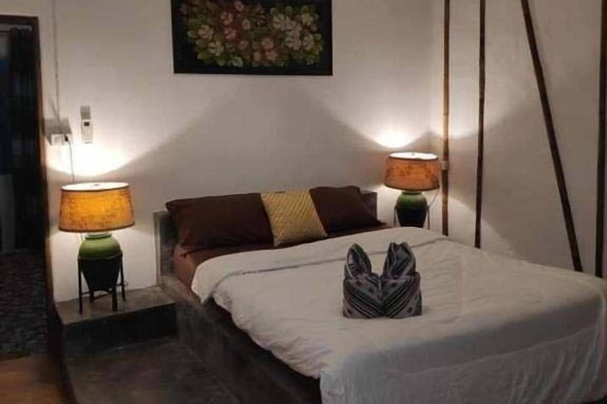 Ein Hotelzimmer mit einem Bett, zwei Nachttischlampen, einem Wandbild und einem kleinen Hocker.