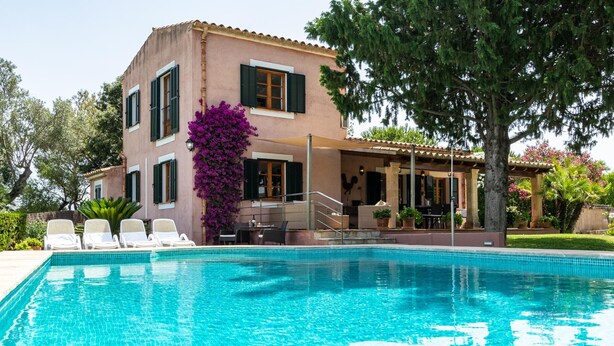 Una piscina con sillas de descanso, un porche cubierto y un edificio con persianas.
