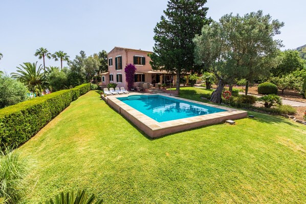 A two-story house with a swimming pool surrounded by well-maintained lawns and trees.