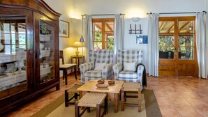 Una sala de estar acogedora con un mueble de madera, sillones a cuadros, una mesita de centro de madera y vistas a través de una puerta de madera.