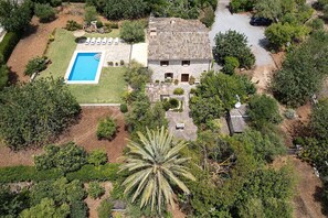 Ilmakuva kiinteistöstä, jossa on uima-allas, kivitalo ja ympäröivää vihreää kasvillisuutta.
