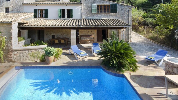 A stone building with a swimming pool, outdoor seating, and lush greenery.