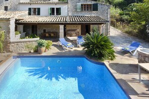Un edificio de piedra con piscina, mobiliario de exterior y exuberante vegetación.