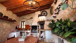 A rustic stone kitchen with a round table, wooden chairs, and a hanging light fixture.