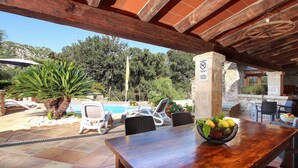 An outdoor patio area with a wooden table, chairs, a pool, and a stone wall.