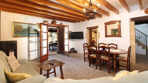 A cozy living room with wooden beams, a TV, a dining table with chairs, and a sofa.