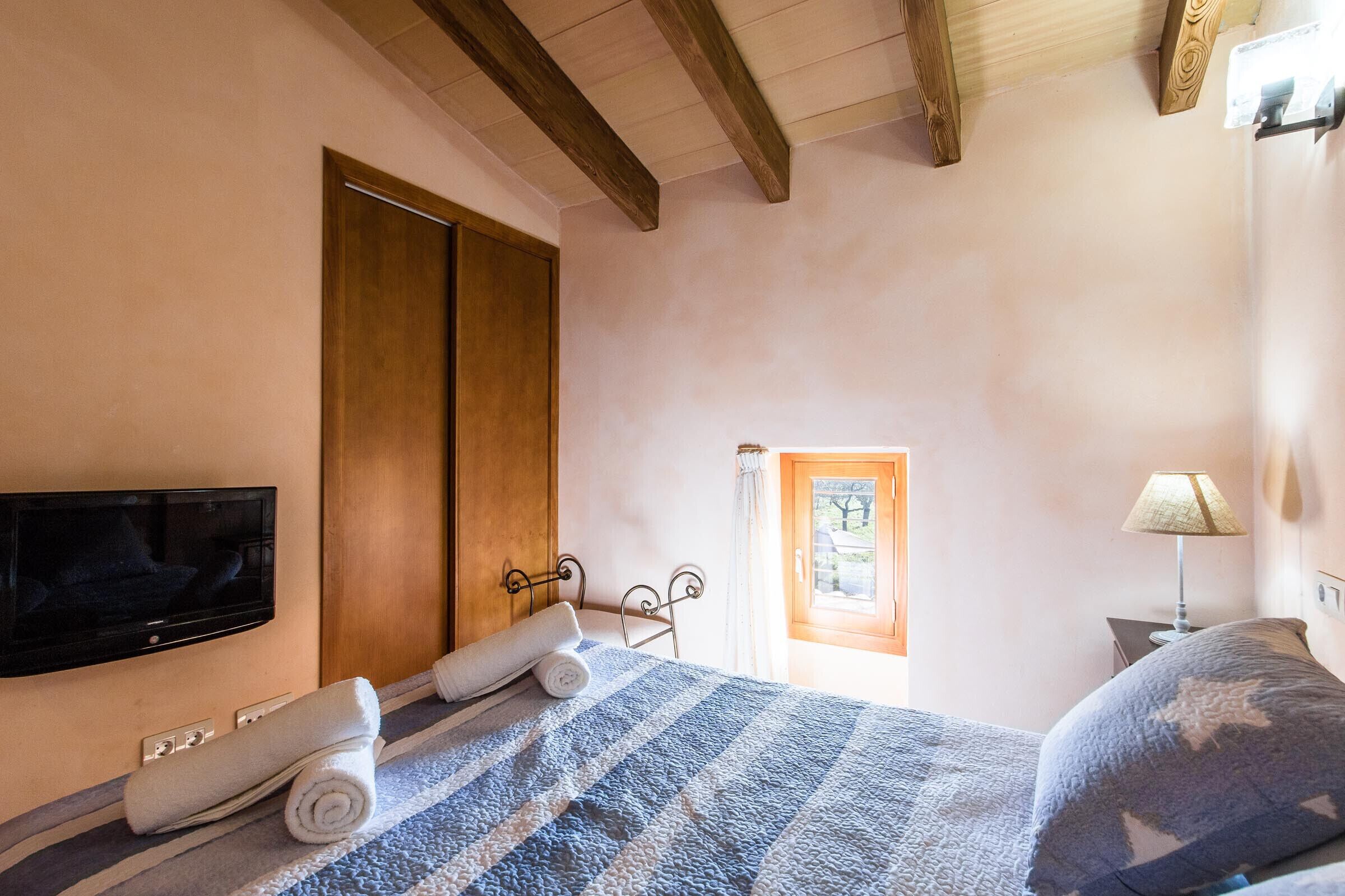 A bedroom with a bed, a TV mounted on the wall, a window with a view, and a door.