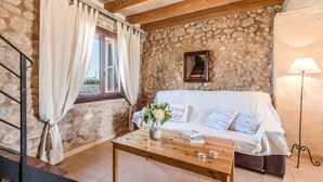 A cozy room with a stone wall, a white sofa, a wooden coffee table, and a window with curtains. - Cas FRARE. Respecting roots with style (Buger)