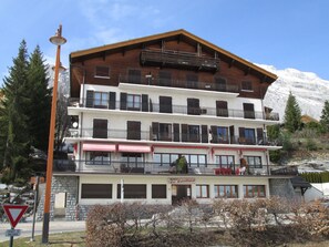 A multi-story hotel with balconies, a restaurant on the ground floor, and a mountain backdrop.