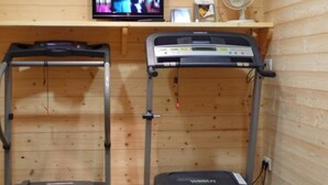 Une pièce équipée de deux tapis de course, d’un téléviseur posé sur une étagère en bois et d’un ventilateur.