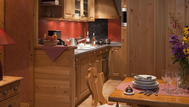 Un intérieur en bois comprenant une cuisine et un coin repas, avec des meubles de rangement en bois, une table à manger dressée avec des assiettes et des verres, et une petite plante posée sur la table.