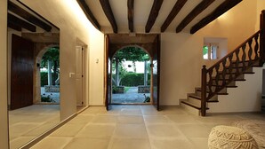 Un couloir avec un escalier en bois, un grand miroir et une vue sur un jardin extérieur.