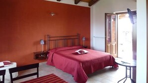 Une chambre avec un plafond en bois, un lit recouvert d’une couverture rouge, une table de chevet avec une lampe et une fenêtre donnant sur l’extérieur.