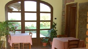 Un espace repas avec des tables et des chaises, une grande fenêtre en arc de cercle et des plantes en pot.