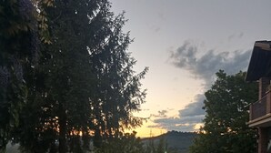 Un espace extérieur aménagé avec des tables et des chaises, entouré d’arbres et offrant une vue sur le coucher de soleil.