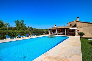 Une piscine rectangulaire à l’eau bleue, entourée d’une terrasse en béton. Des chaises longues bleues sont alignées le long du bord de la piscine.