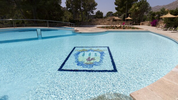 A swimming pool with a mosaic design, surrounded by trees and lounge chairs. - GRAN VORAMAR CALA. 200 m2 pool and 6 bedrooms (Cala San Vicente)