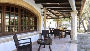 An outdoor patio with wicker furniture, a stone table, and a large arched window. - GRAN VORAMAR CALA. 200 m2 pool and 6 bedrooms (Cala San Vicente)