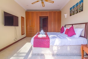 A bedroom with a bed, a ceiling fan, a TV, wooden wardrobe, and artwork on the wall. - 2 Bed Majestic Villa Near Beach (Pattaya)