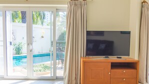 A room with a sliding glass door leading to a pool, a wooden TV stand, and a beige curtain. - 2 Bed Majestic Villa Near Beach (Pattaya)