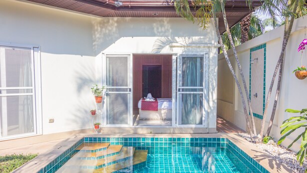 A swimming pool with a tiled edge, a covered seating area with a red and white striped cushion, and potted plants. - 2 Bed Majestic Villa Near Beach (Pattaya)