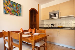 A dining table with chairs, a wooden door, and a kitchen with cabinets and a microwave.