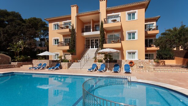 Ein mehrstöckiges Hotel mit Schwimmbad, Liegestühlen und einer Treppe zum Eingang.