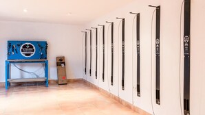 Una habitación con una fila de esquíes negros en la pared, una mesa azul con equipo de ciclismo y una caja de cartón etiquetada 