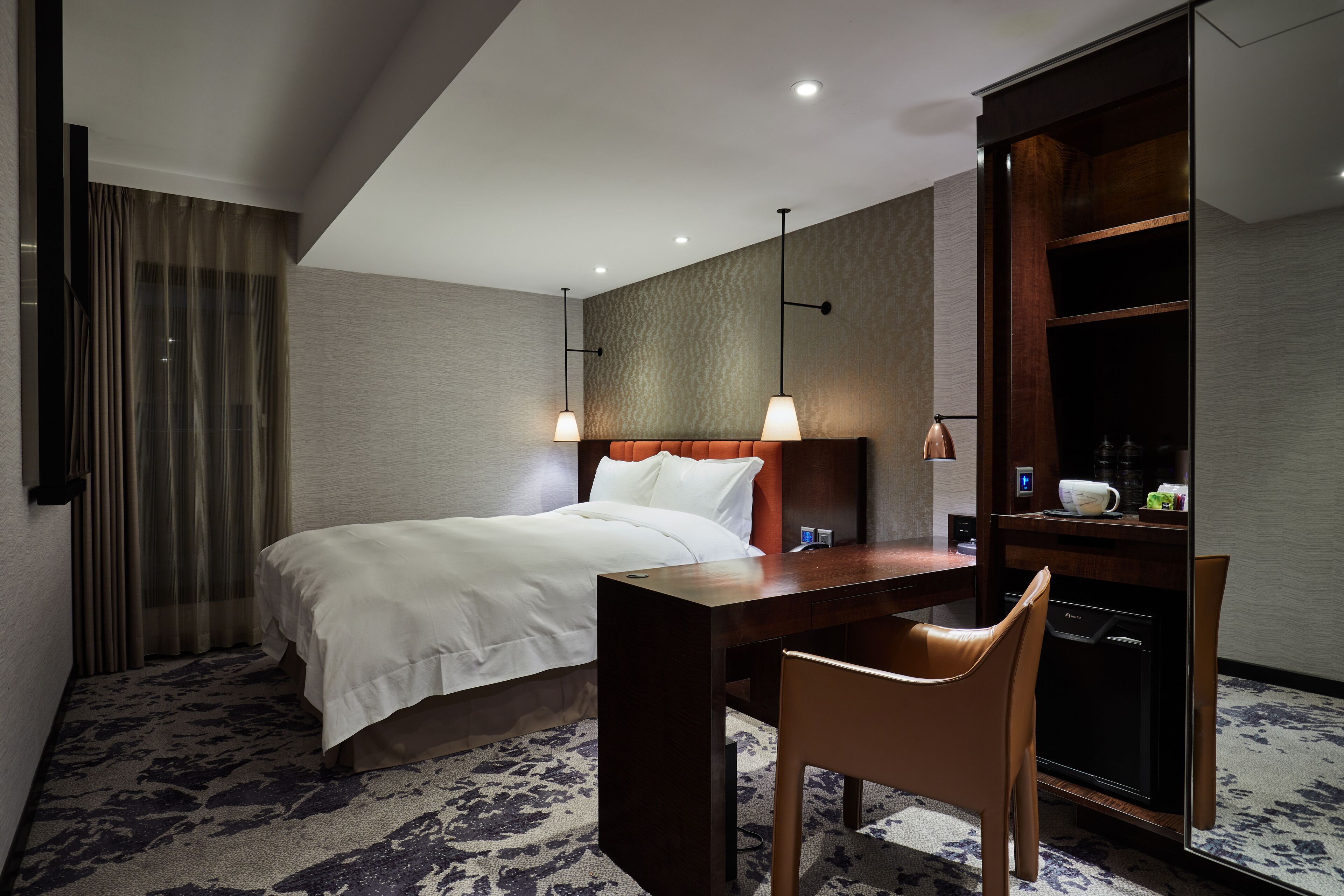 A hotel room with a bed, a desk, a chair, a wardrobe, and a coffee machine.