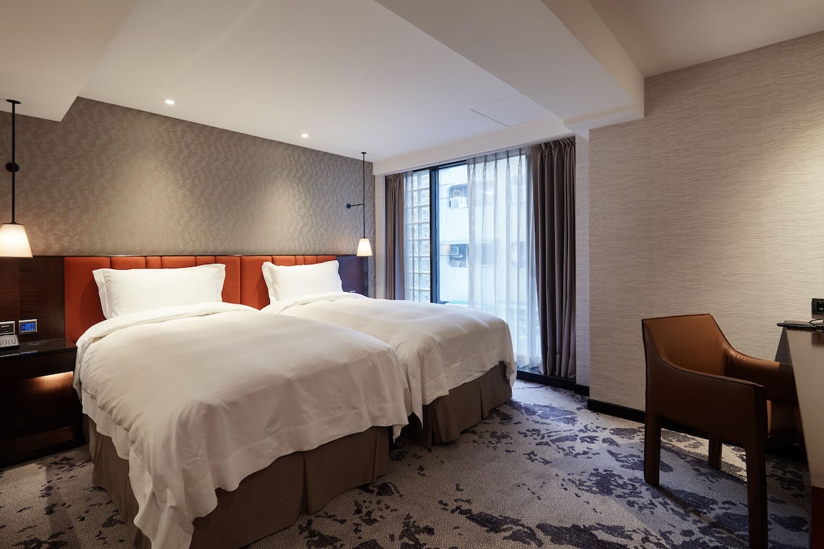 Une chambre d’hôtel avec un lit double, un bureau avec une chaise, un téléphone et une fenêtre avec des rideaux.