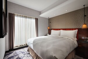 Habitación de hotel moderna con una cama grande, cabecera de madera, escritorio con teléfono y un ventanal con cortinas.