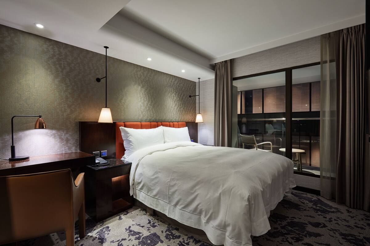 Une chambre d’hôtel avec un lit, un bureau, une chaise et une vue sur l’extérieur.