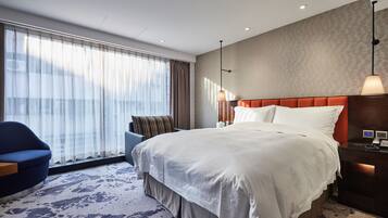 A hotel room with a large bed, a desk, a chair, and a large window with curtains.