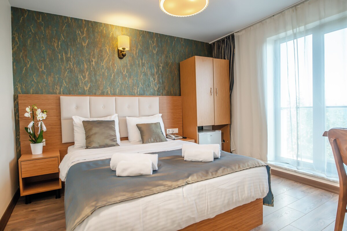 A neatly made bed with a headboard, a nightstand with a lamp, a wardrobe, and a window with curtains.