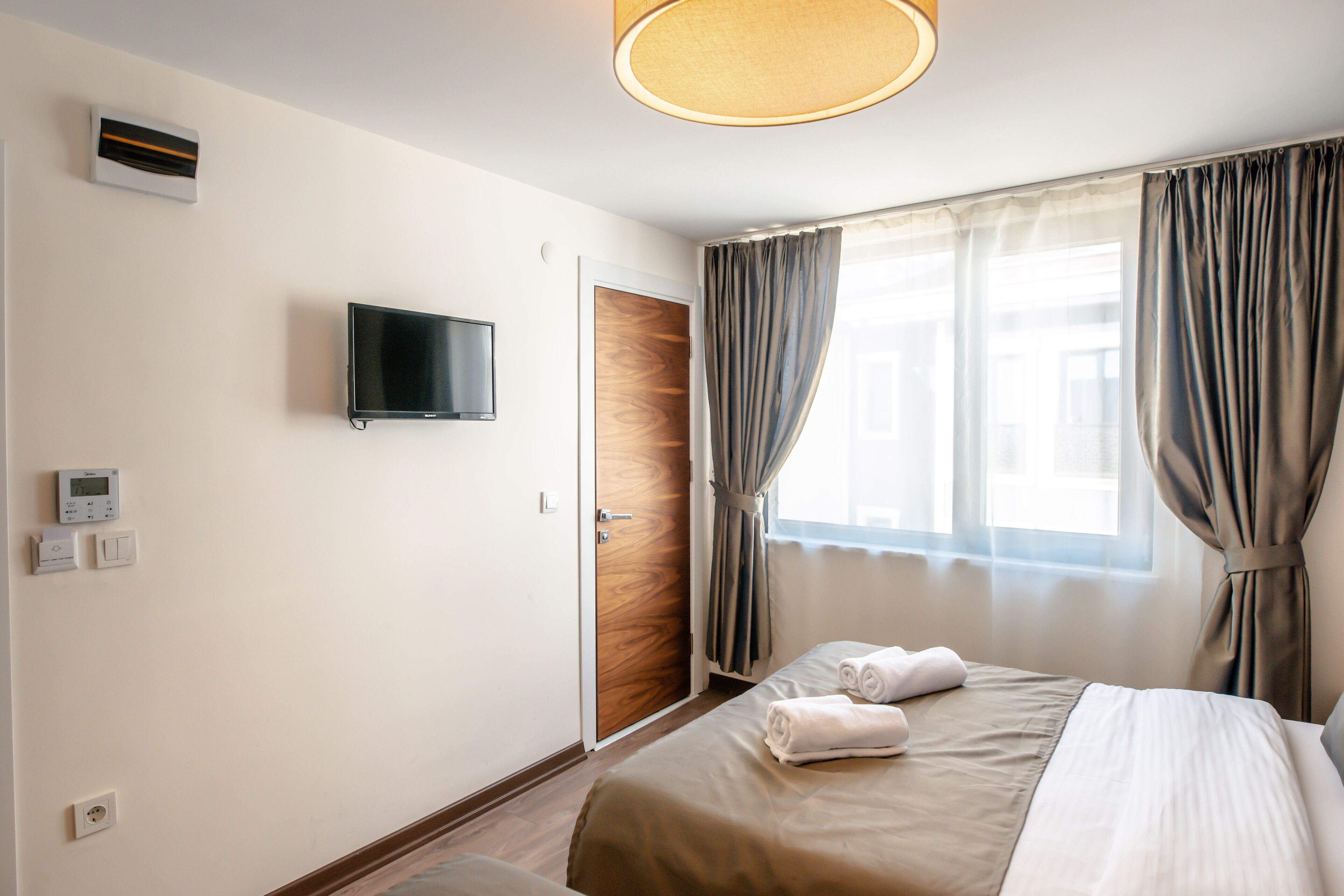 A hotel room with a bed, a television, a wooden door, and a window with curtains.