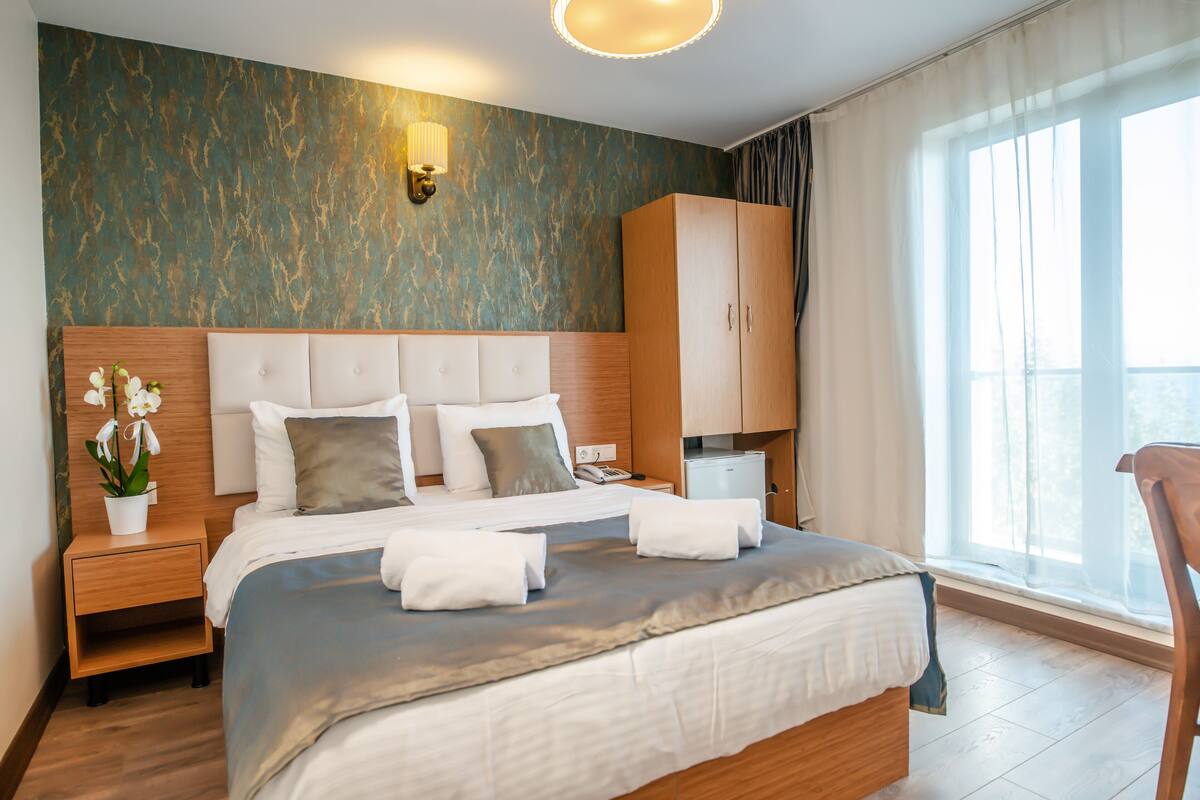 Ett hotellrum med en stor säng, ett nattduksbord, en garderob och ett fönster med gardiner.