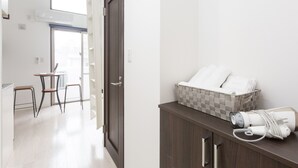 Habitació d'hotel amb un armari de fusta, una taula petita amb dues cadires, un cistell de tovalloles i un assecador a la superfície.