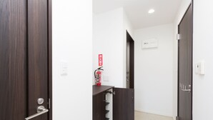 Un passadís amb una porta de fusta, un extintor i un termòstat a la paret.