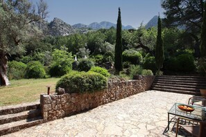 A stone patio with steps leading to a seating area, surrounded by lush greenery and a mountainous backdrop. - PASCOL. Villa over 250 years old in a breathtaking setting (Pollensa)