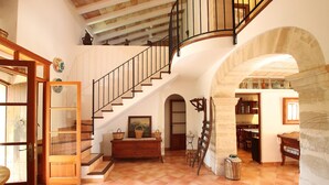 Amplia sala de estar con escalera de madera, comedor y cocina visibles a través de un arco.
