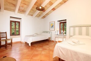 A bedroom with two beds, a wooden chair, a desk with a lamp, and a window with a view of greenery. - PASCOL. Villa over 250 years old in a breathtaking setting (Pollensa)