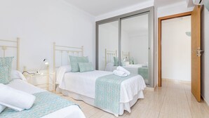 Hotellihuone, jossa on kaksi sänkyä, yöpöytä lampun kanssa, suuri liukuovi ja puuovi.