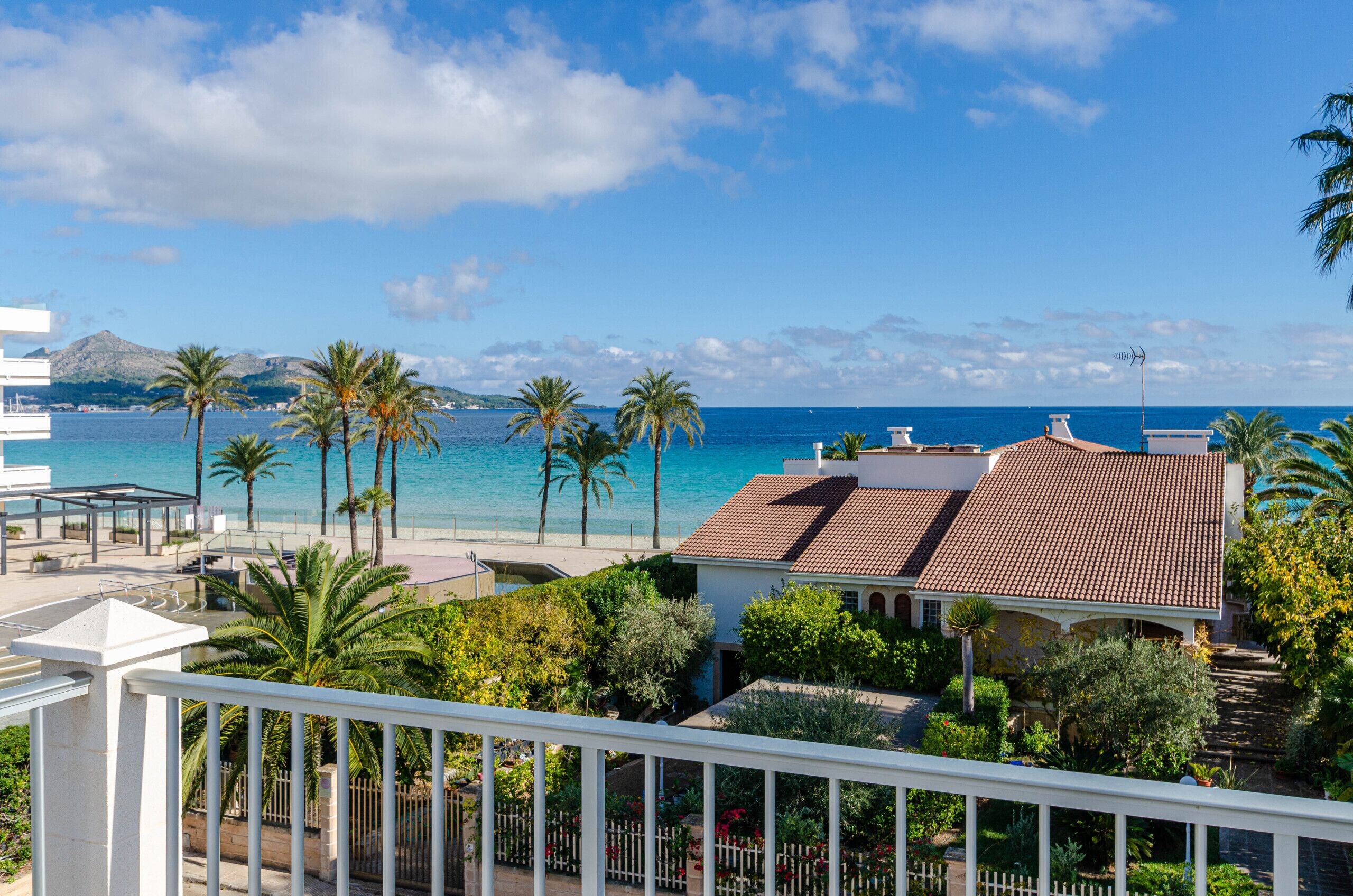 A coastal property with a beach view, palm trees, and a red-tiled roof house.