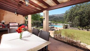 Une terrasse extérieure avec une table et des chaises, un vase de fleurs et une vue sur une piscine et des montagnes.