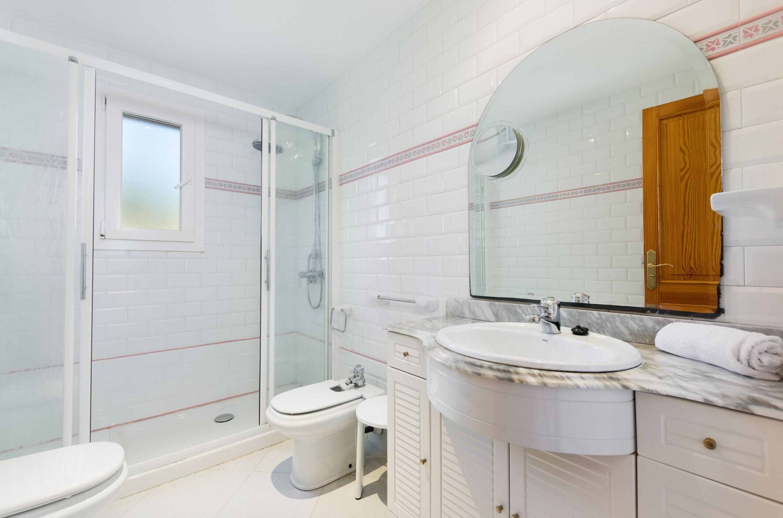 A modern bathroom with a glass-enclosed shower, a white toilet, a sink with a marble countertop, and a large mirror with a wooden cabinet above it.