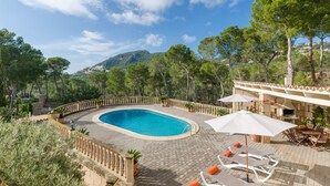 A swimming pool surrounded by a wooden deck, with outdoor seating and a view of a mountainous landscape. - YourHouse Binifat, spacious house overlooking Puerto de Andratx (Andratx)