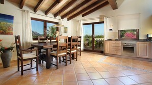 A dining area with wooden chairs and a table, a kitchen with wooden cabinets and an oven, and large windows with a view of greenery. - LLOP. Magnificent villa with sauna (Pollensa)