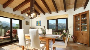 A dining area with a wooden table and chairs, large windows with mountain views, and a wooden cabinet with dishes. - LLOP. Magnificent villa with sauna (Pollensa)