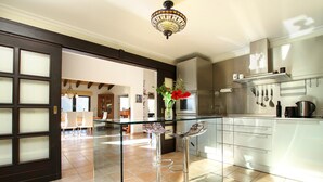 A modern kitchen with a glass-top bar stool, stainless steel appliances, and a hanging pot rack. - LLOP. Magnificent villa with sauna (Pollensa)