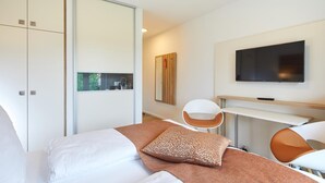 A modern hotel room with a bed, a TV, a desk, and a chair. - VR-Serviced Apartments Obergeis (Neuenstein)